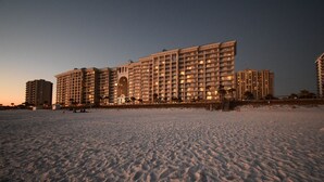 Un grand hôtel à plusieurs étages, doté de balcons, situé sur une plage de sable.