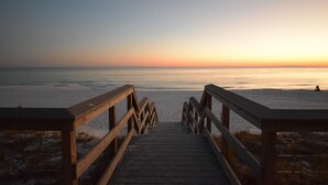 Une promenade en bois menant à une plage, avec un coucher de soleil en arrière-plan.