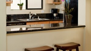 A kitchen with a window, a sink, two stools, and a potted orchid. - Romantic Beachfront Getaway (Maalaea Bay)