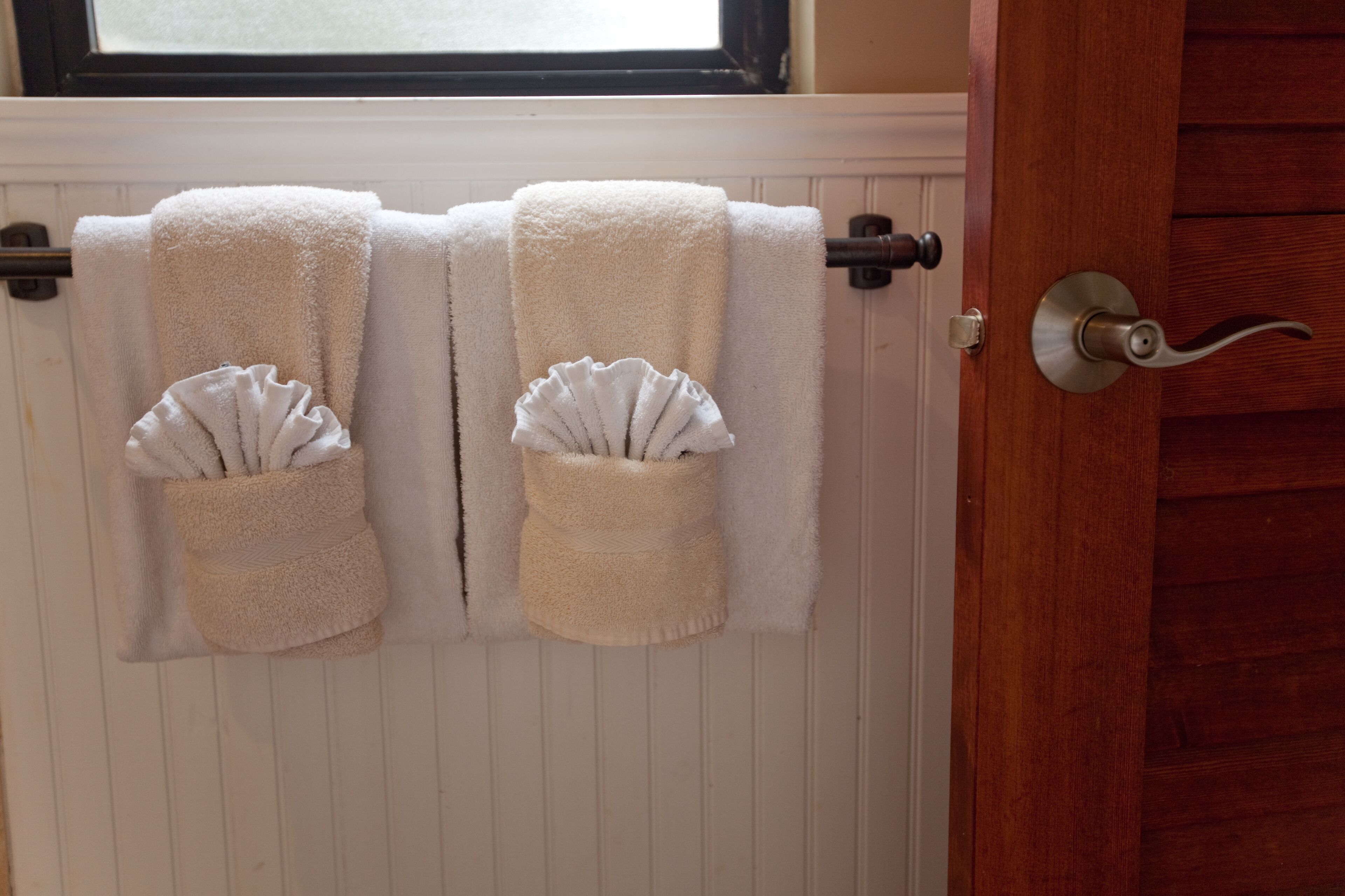 A bathroom with two towels hanging on a rack, a wooden door, and a window above the towels.