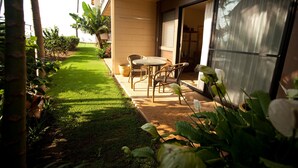 A patio with a table and chairs, a small garden, and a sliding glass door leading to an interior space. - Romantic Beachfront Getaway (Maalaea Bay)