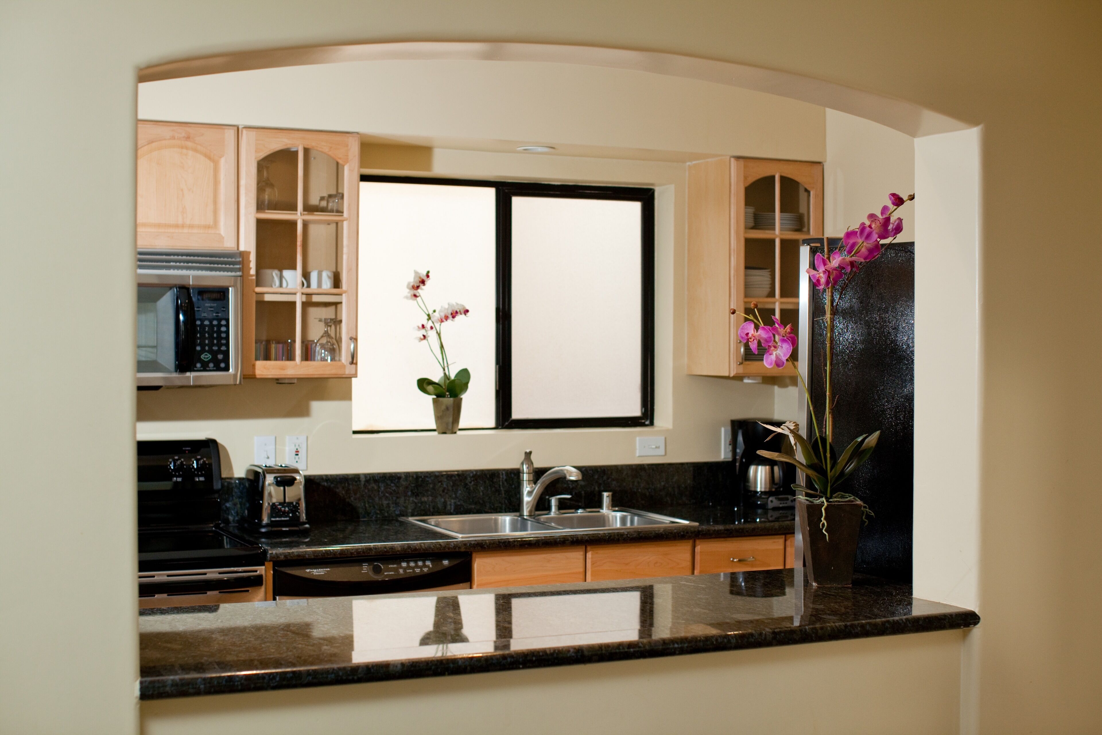 A kitchen with a double sink, wooden cabinets, and a window with a potted orchid.