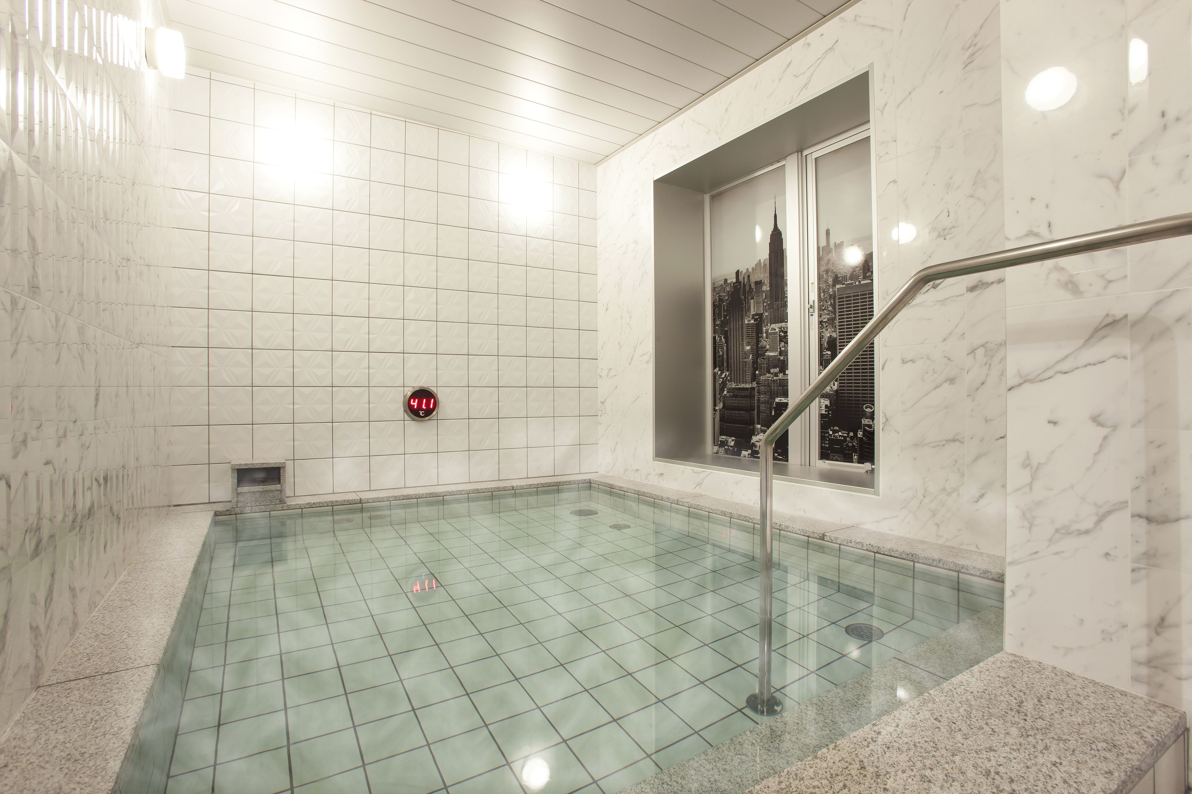 A modern indoor pool with a cityscape view through a window, marble walls, and a digital clock.