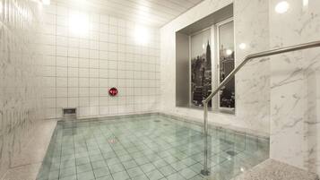 A modern indoor pool with a cityscape view through a window, marble walls, and a digital clock.