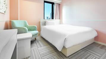 A modern hotel room with a large bed, a seating area with a chair, a small table, and a window with a view of the city.