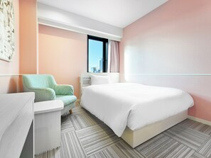 Una habitación de hotel moderna con una cama grande, una zona de estar con una silla, una mesita y un ventanal con vistas a la ciudad.