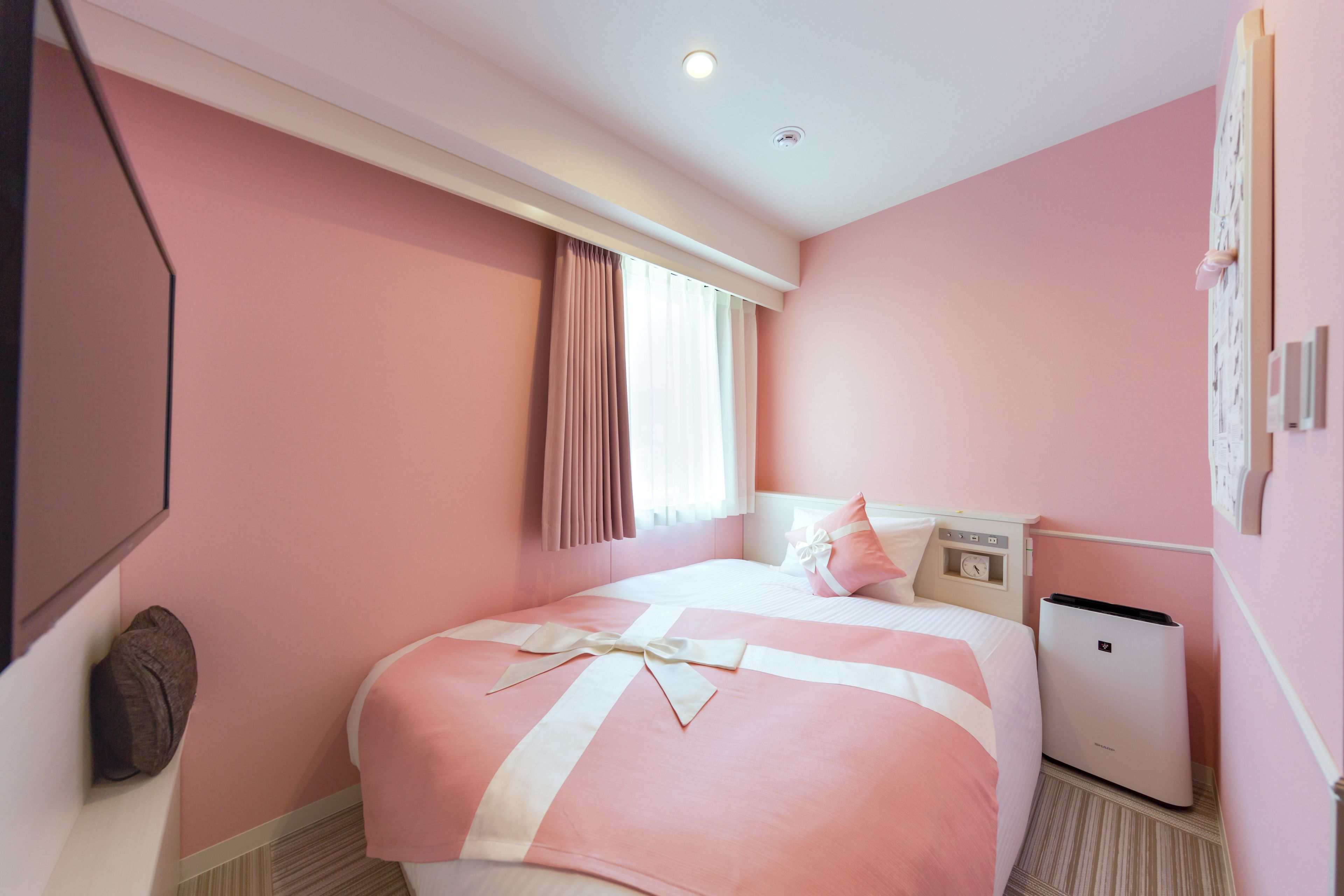 A pink-themed hotel room with a bed, bedside table, and a small heater.