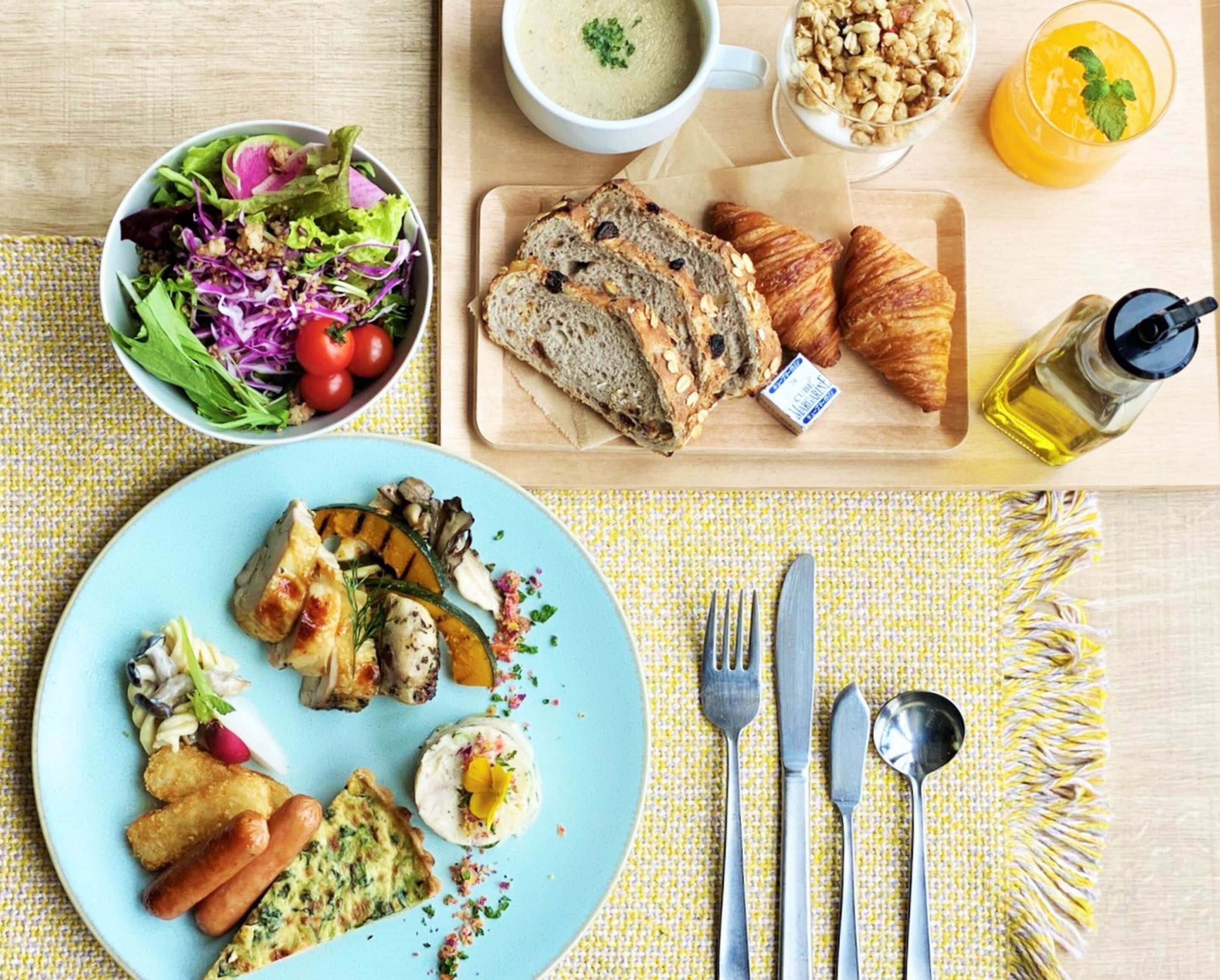 A breakfast setting with a plate of food, a bowl of salad, croissants, and a glass of orange juice.
