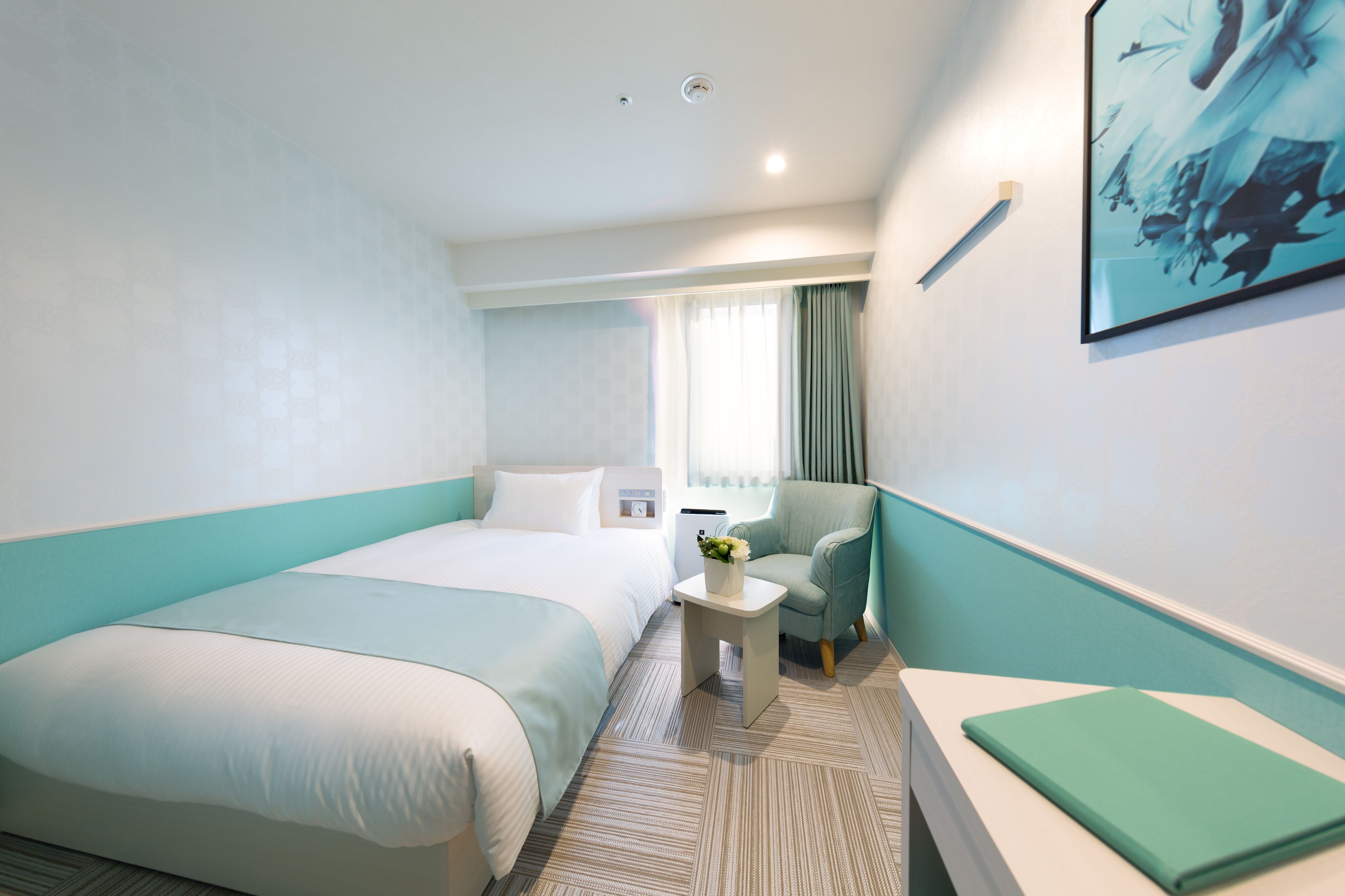 A hotel room with a large bed, a small table with a vase of flowers, a chair, and a painting on the wall.
