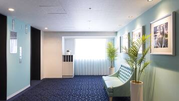 Eine Hotelhalle mit einem gemusterten Teppich, einer Sitzecke mit gepolsterten Bänken, einer Topfpflanze und gerahmten Bildern an der Wand.