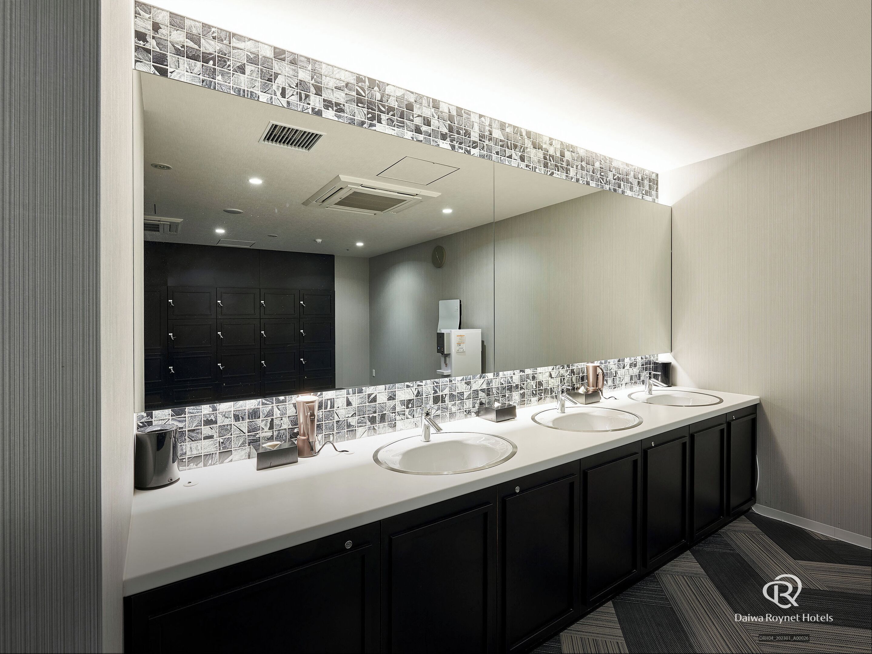 Un baño moderno con un mueble de tocador largo, tres lavamanos y un espejo grande.