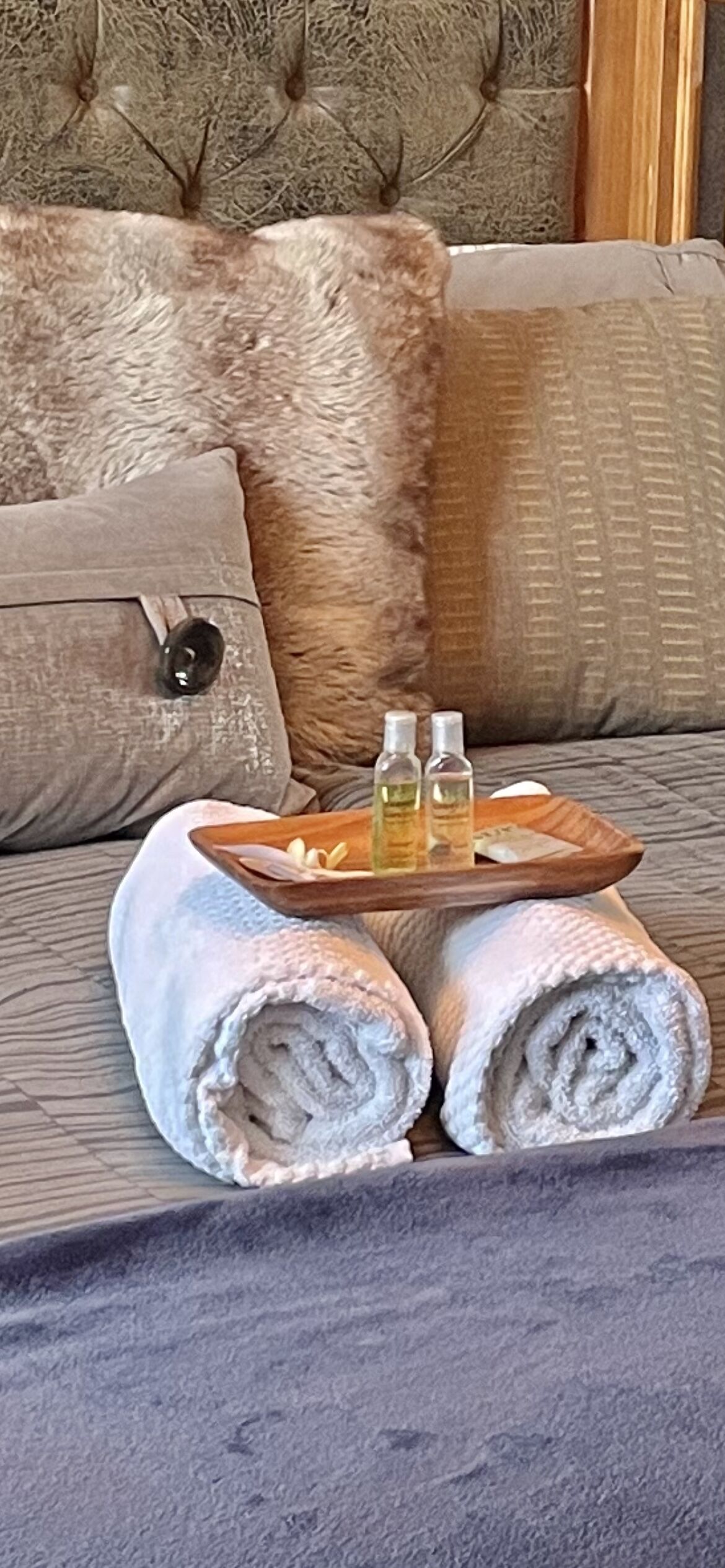 Una cama bien hecha con toallas enrolladas y dos botellas de loción sobre una bandeja.