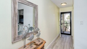 A hallway with a wooden console table, a mirror with a rustic frame, and a door leading to a balcony with a view of palm trees. - Condo# 309 Fully renovated 1b/1b unit with great views of the gulf (Sarasota)