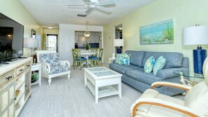A living room with a sofa, chairs, a coffee table, and a television. There is a ceiling fan, a painting on the wall, and a lamp. - Condo# 309 Fully renovated 1b/1b unit with great views of the gulf (Sarasota)