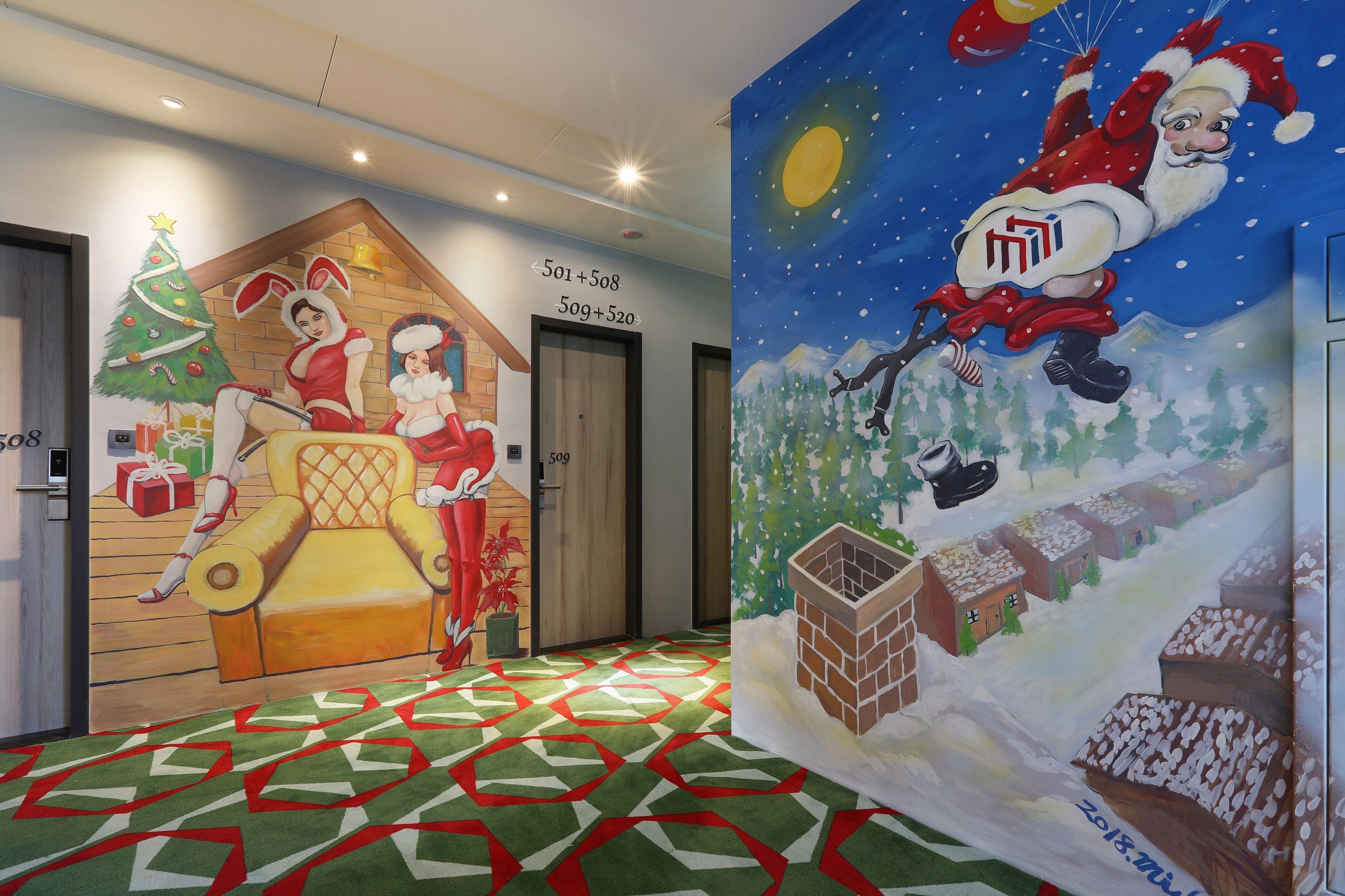 A hotel corridor with a Christmas-themed mural, a patterned carpet, and doors numbered 508 and 509.