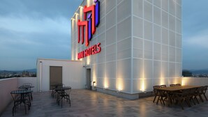 A modern hotel with a prominent signage, outdoor seating area, and a view of the cityscape. - Mini Hotels Taichung Station Branch (Taichung)