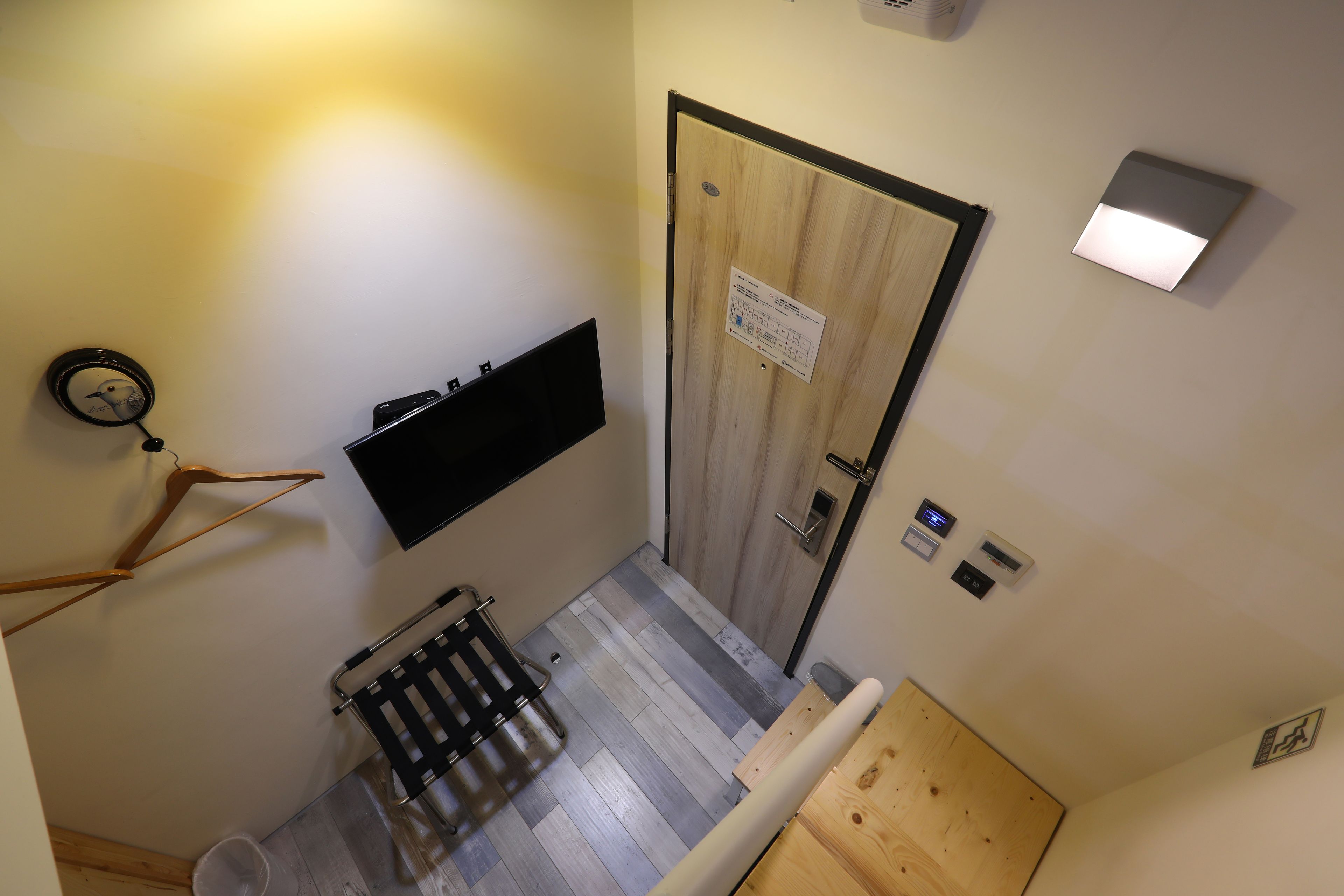 A hallway with a wooden door, a wall-mounted TV, a radiator, and a small trash bin.