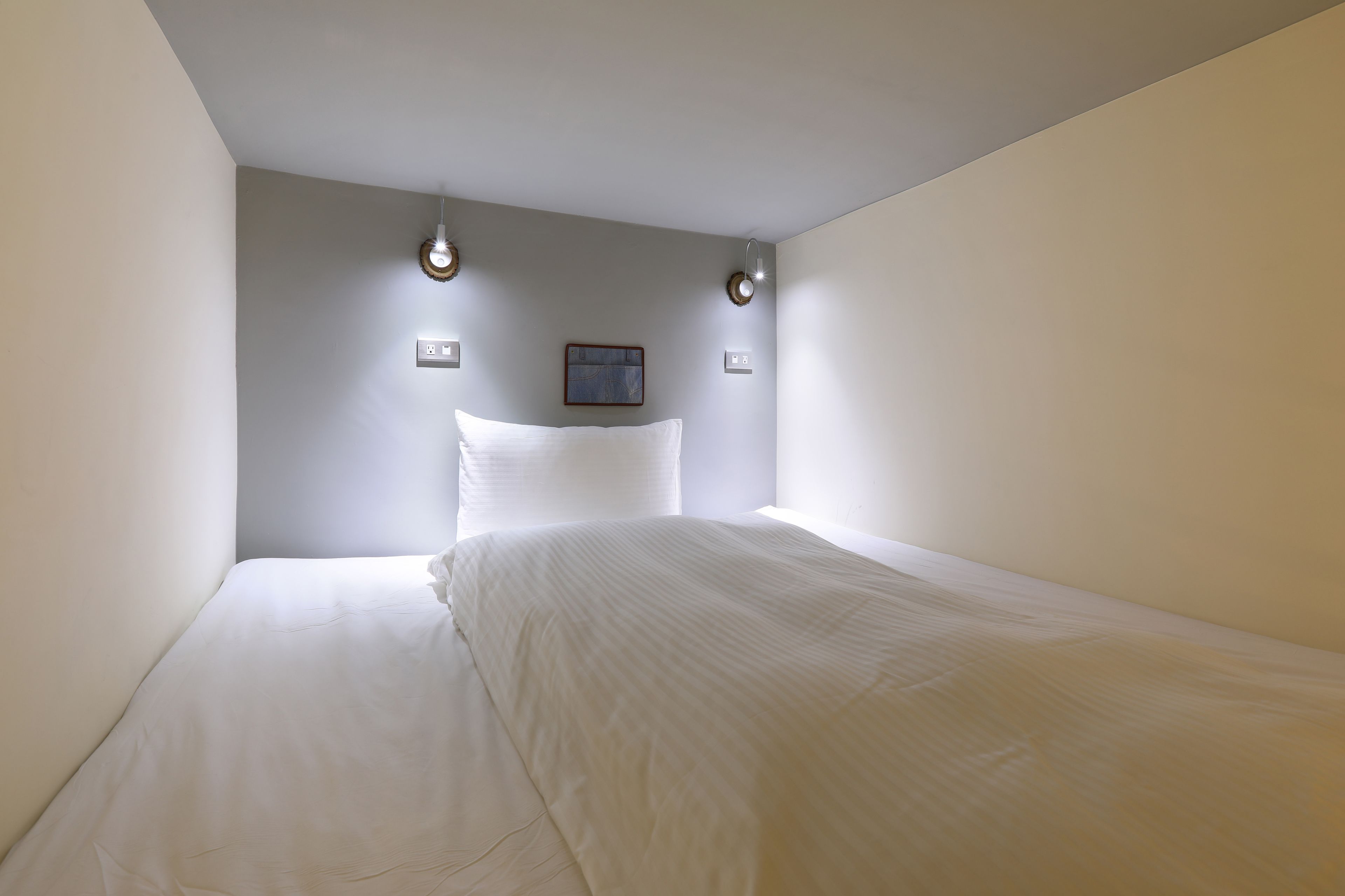 A minimalist hotel room with a large bed, two wall-mounted lights, and a small framed picture on the wall.