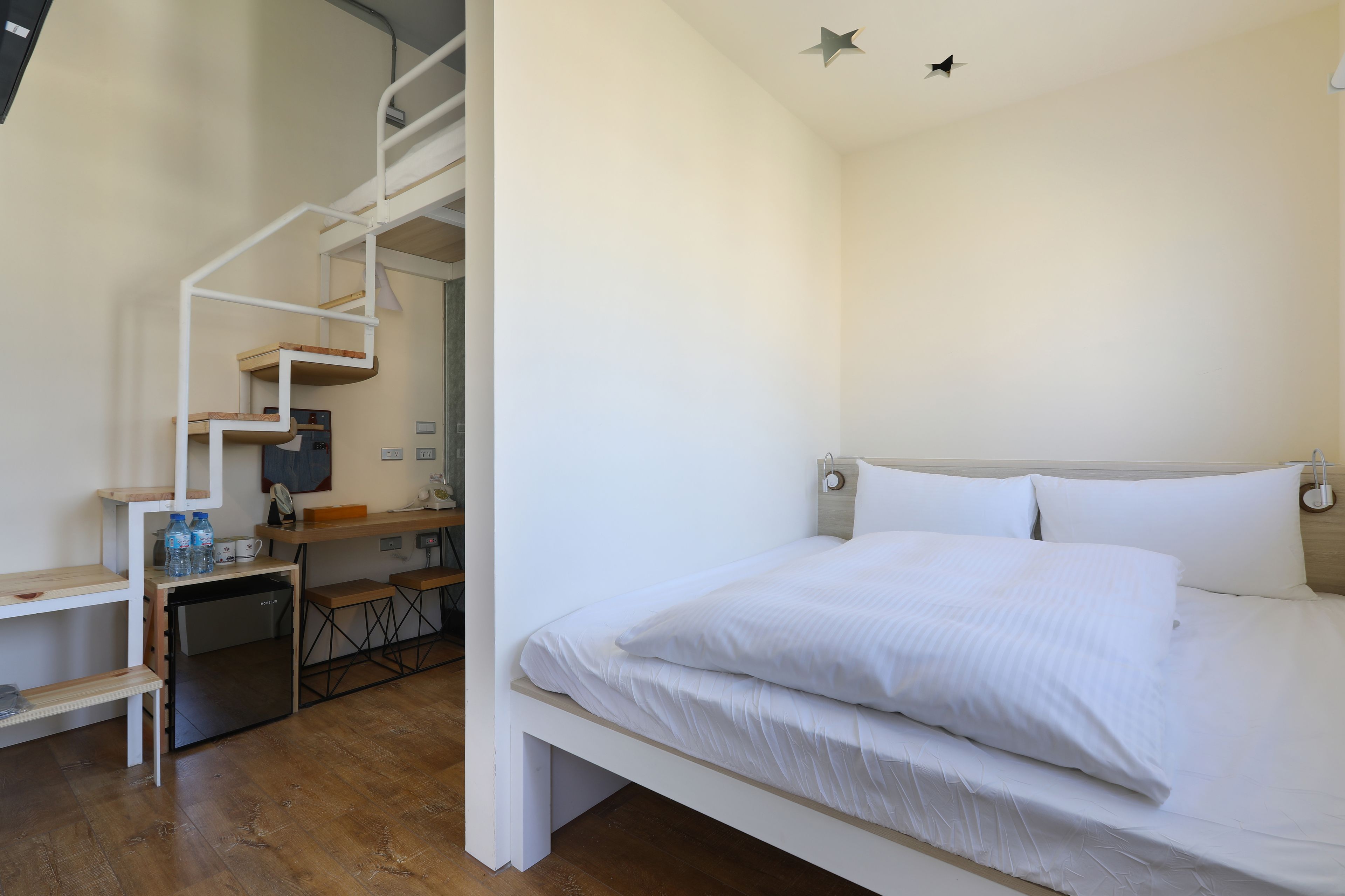 Une chambre avec un lit, un bureau, une chaise, un petit réfrigérateur et un escalier.