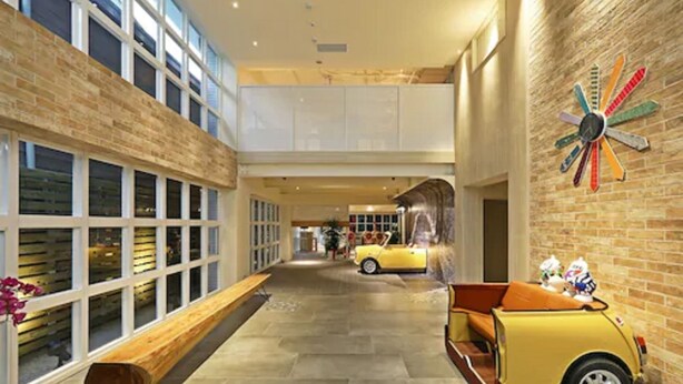 A spacious lobby with a high ceiling, a bench along the wall, a yellow convertible car, and a colorful clock on the wall. - Mini Hotels Taichung Station Branch (Taichung)