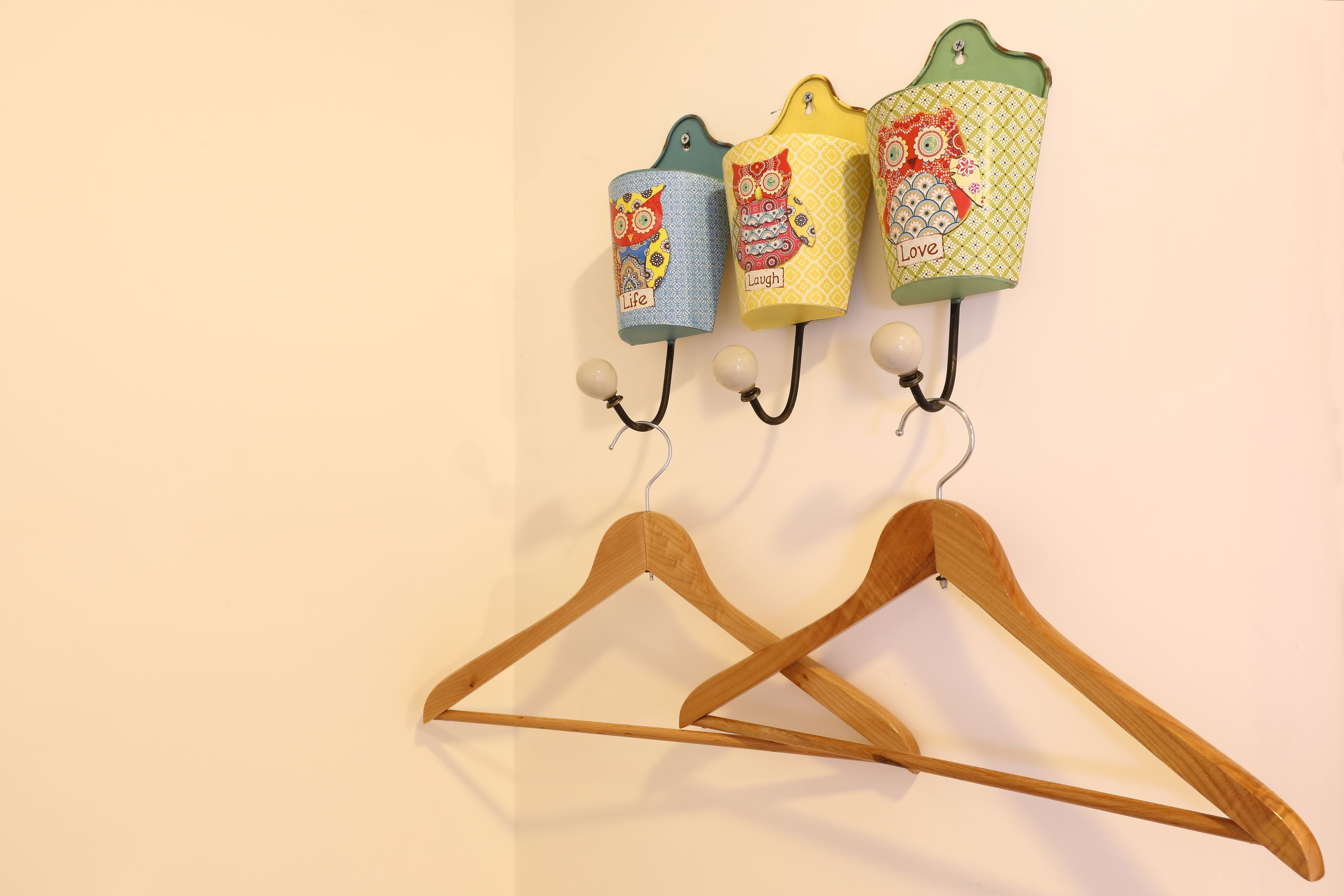 A wall-mounted rack with three colorful fabric hangers and two wooden hangers.
