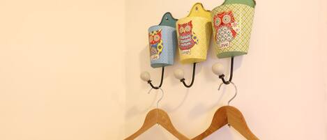 A wall-mounted rack with three colorful fabric hangers and two wooden hangers.