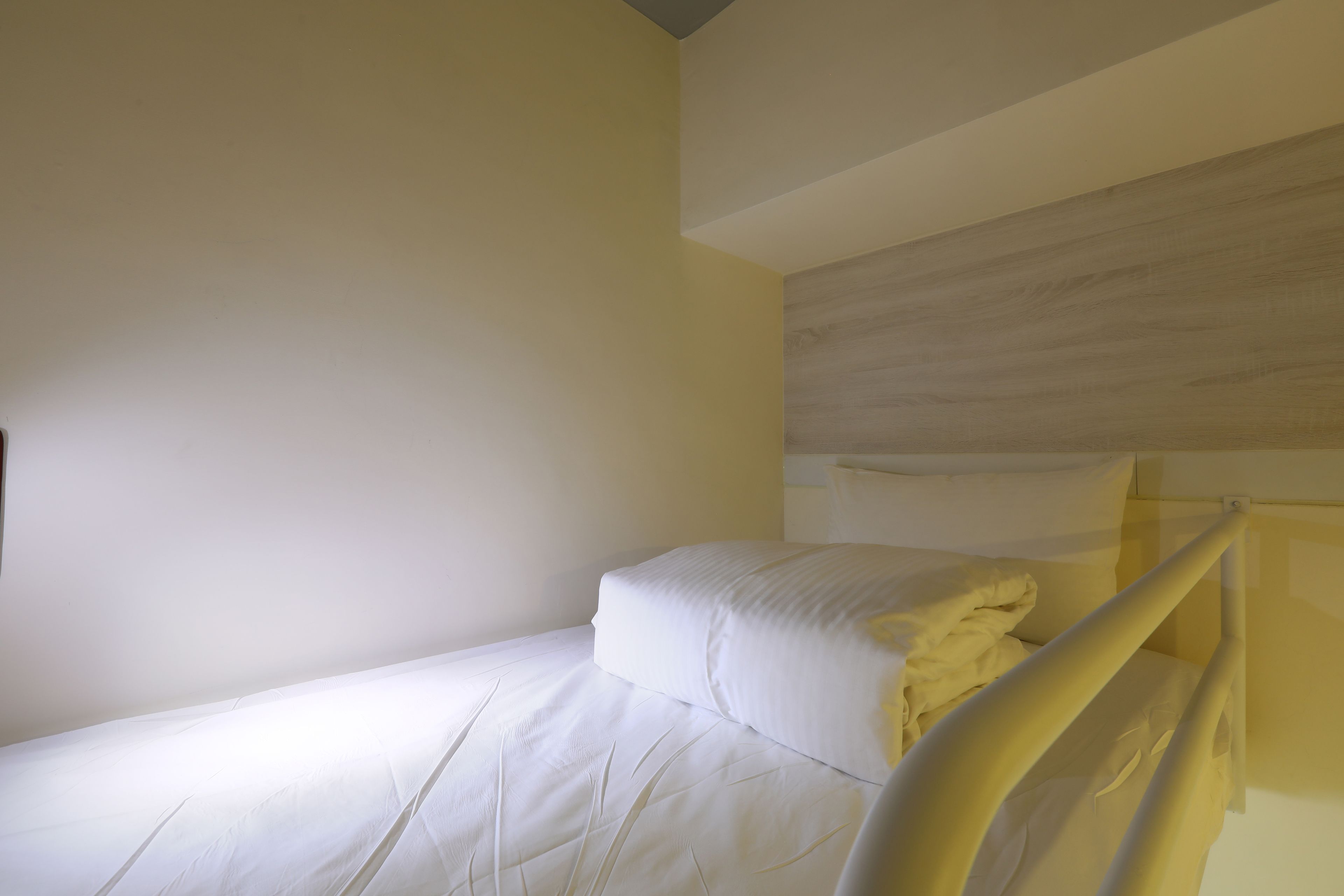 A single bed with white bedding in a room with plain walls and a wooden headboard.