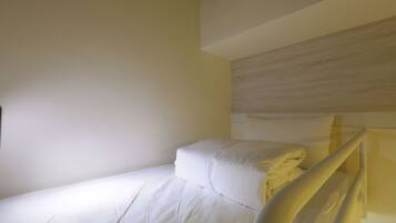 A single bed with white bedding in a room with plain walls and a wooden headboard.