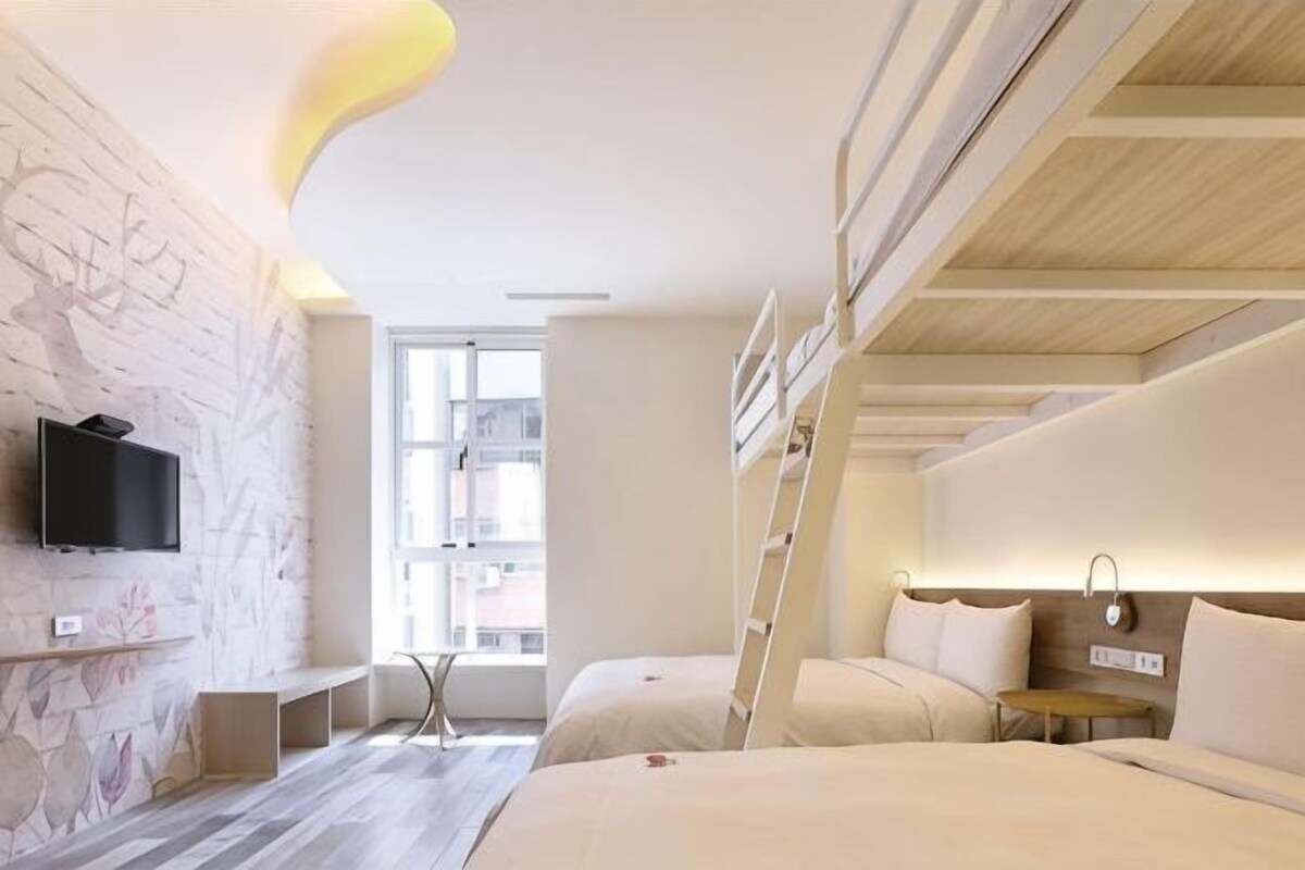 Een hotelkamer met een televisie, een raam, een bed, een nachtkastje en een wandlamp.