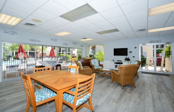 A spacious indoor area with a wooden dining table and chairs, wicker sofas, and a TV screen.