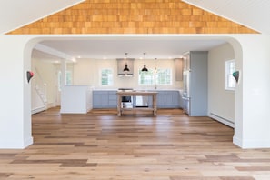 Cocina amplia con piso de madera, una isla central, iluminación colgante y vistas al exterior a través de ventanas grandes.