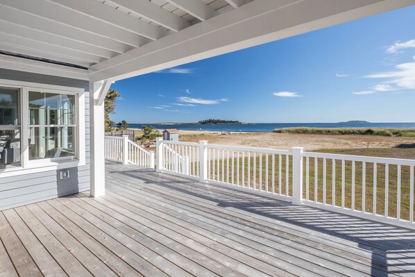 A wooden deck with a white railing overlooking a beach and ocean.