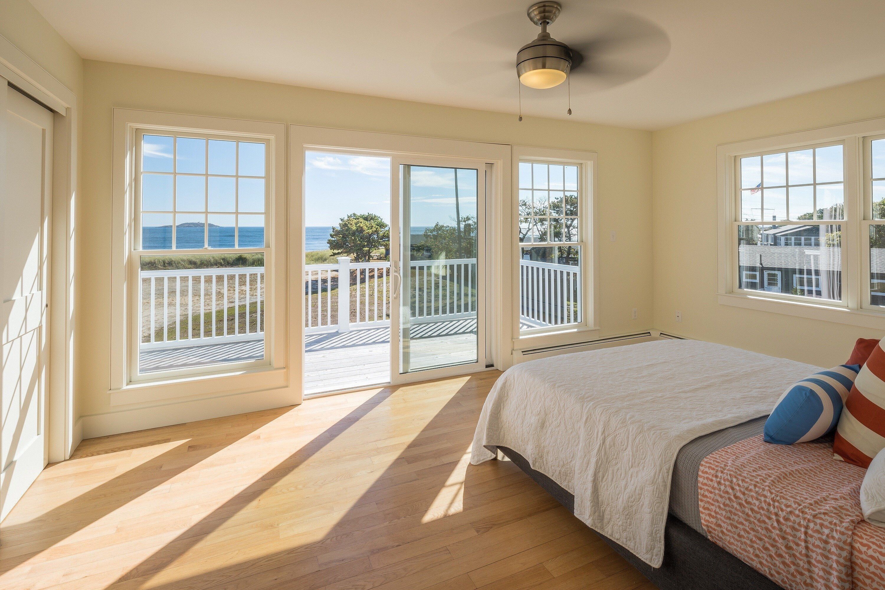 A bedroom with a large bed, a view of the outdoors through sliding glass doors, and a ceiling fan.