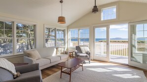 Un salón espacioso con un gran ventanal con vistas a la playa, un sofá acogedor, una silla y una mesa de centro.