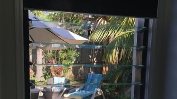 Un área exterior con cerramiento de vidrio, piscina, sillas de descanso y sombrillas.