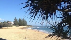 Una playa arenosa con una valla de madera, algunas personas y un edificio al fondo.