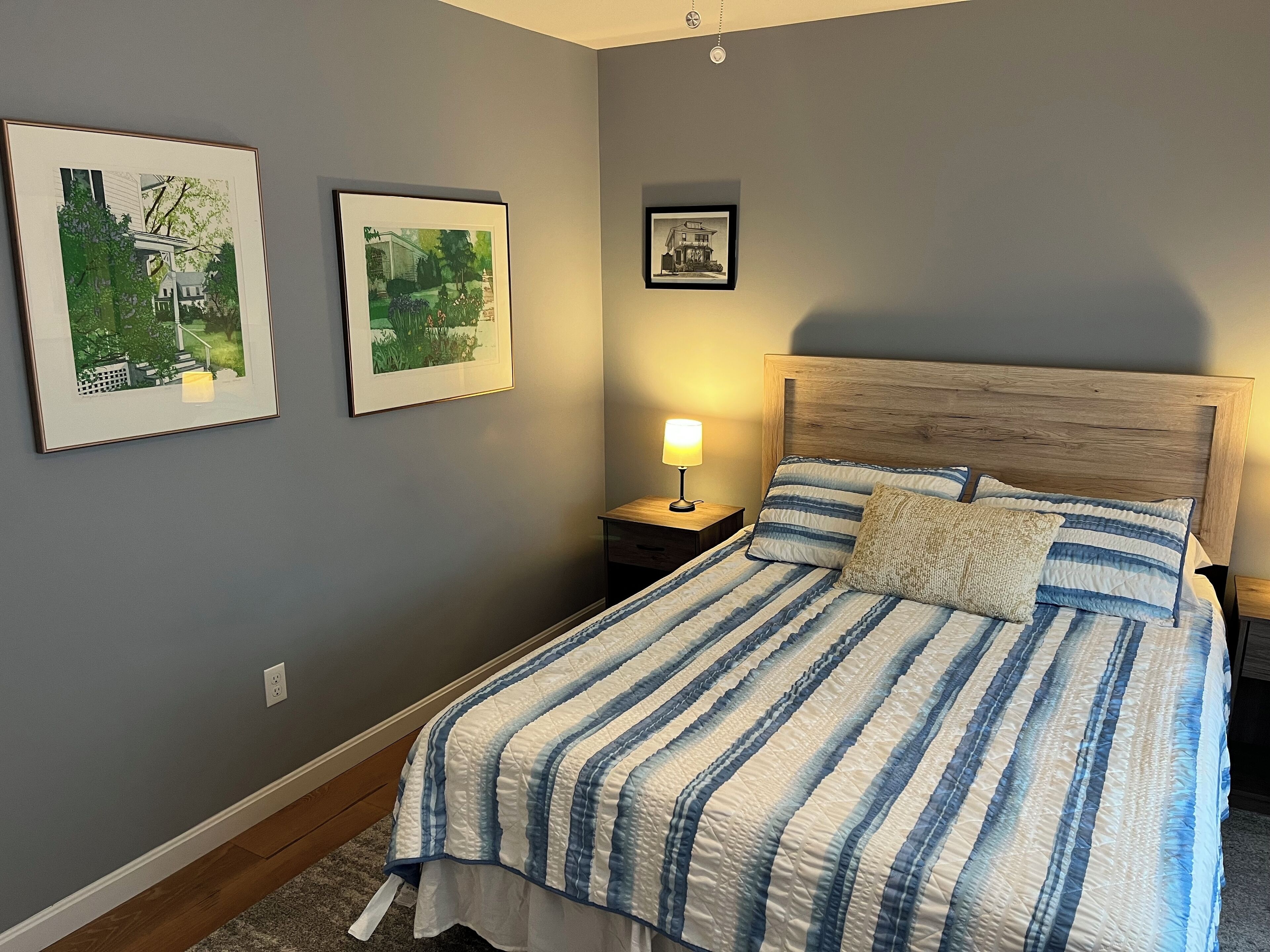 Ein Schlafzimmer mit einem Bett, einem Nachttisch, einer Lampe und zwei gerahmten Bildern an der Wand.