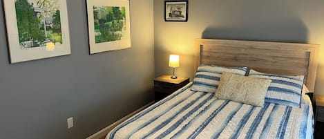 Ein Schlafzimmer mit einem Bett, einem Nachttisch, einer Lampe und zwei gerahmten Bildern an der Wand.