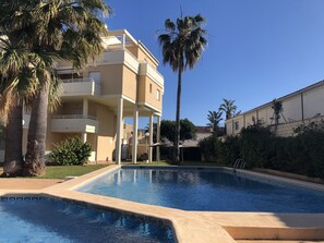 Ein Schwimmbecken mit einer gefliesten Kante, umgeben von Palmen und einem mehrstöckigen Gebäude mit Balkonen.