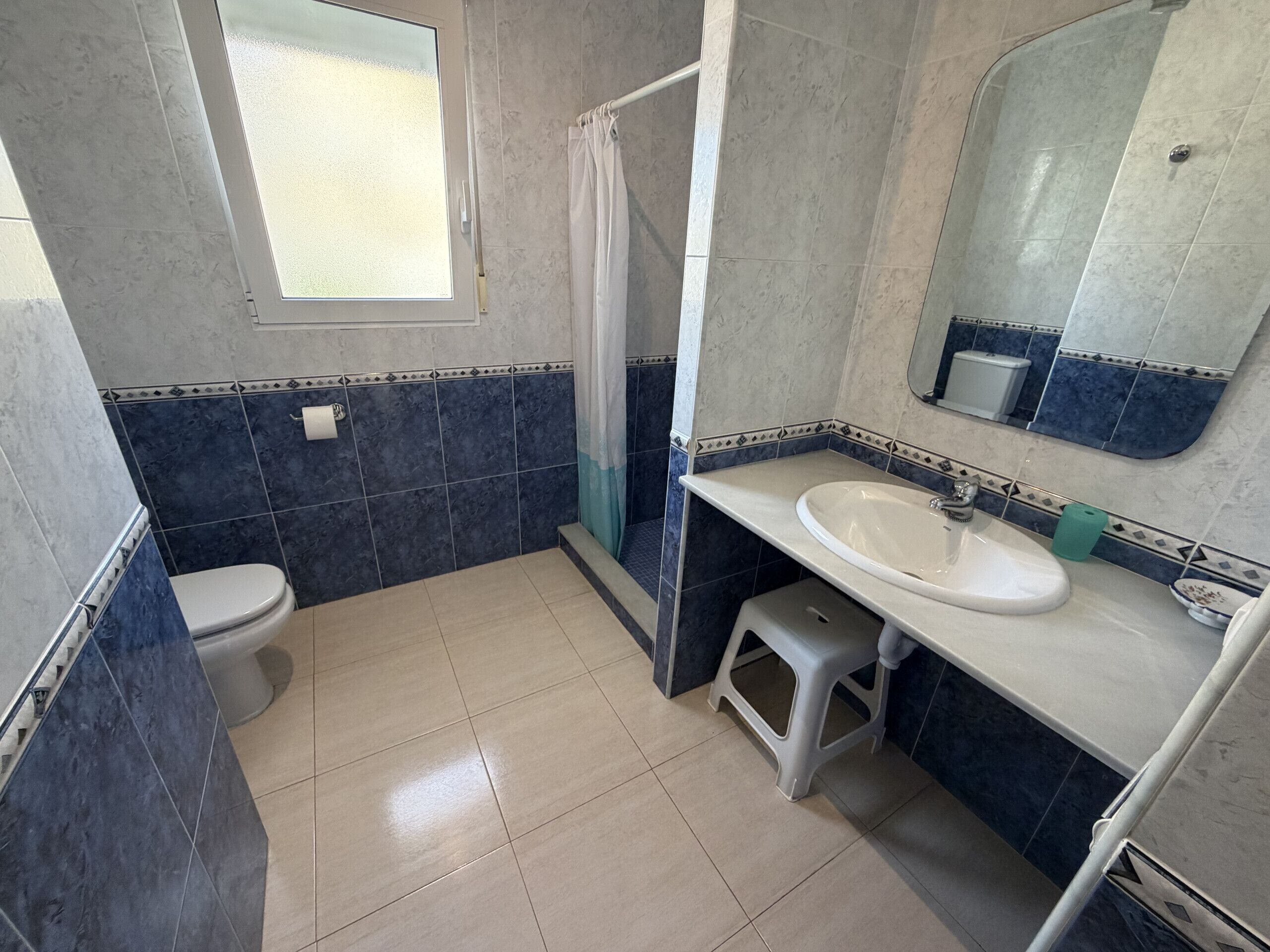 Une salle de bain avec des toilettes, un lavabo, une douche et une fenêtre.
