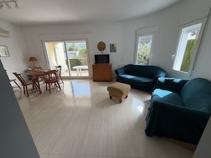 En rummelig opholdsstue med spisebord, stole, sofa, TV-møbel og en skydedør til en udendørs terrasse.
