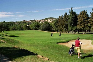 Golfers tee off amidst lush greenery and rolling hills.