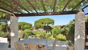 An outdoor patio with a wooden table and chairs, surrounded by stone flooring and greenery.