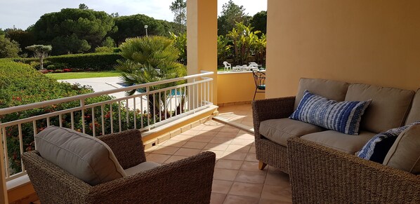 A balcony with wicker furniture and a view of a landscaped garden.