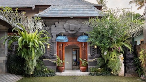 A traditional building with a tiled roof, a wooden entrance, and potted plants. - Kano Sari (Ubud)