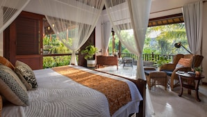 A spacious bedroom with a large bed, a balcony with wicker furniture, and a view of lush greenery. - Kano Sari (Ubud)