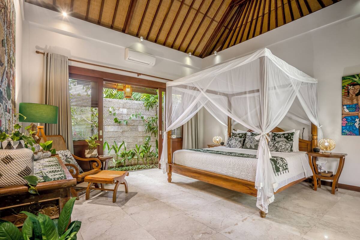 A bedroom with a four-poster bed, a wooden chair, a small table, and a green lamp.