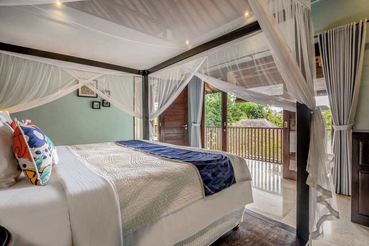 A bedroom with a large bed, a balcony with a view, and a mosquito net.