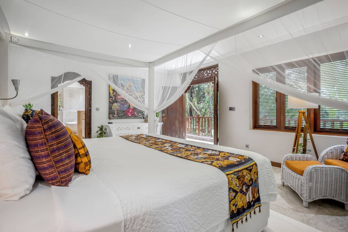 A spacious bedroom with a large bed, white walls, and a view of greenery outside.