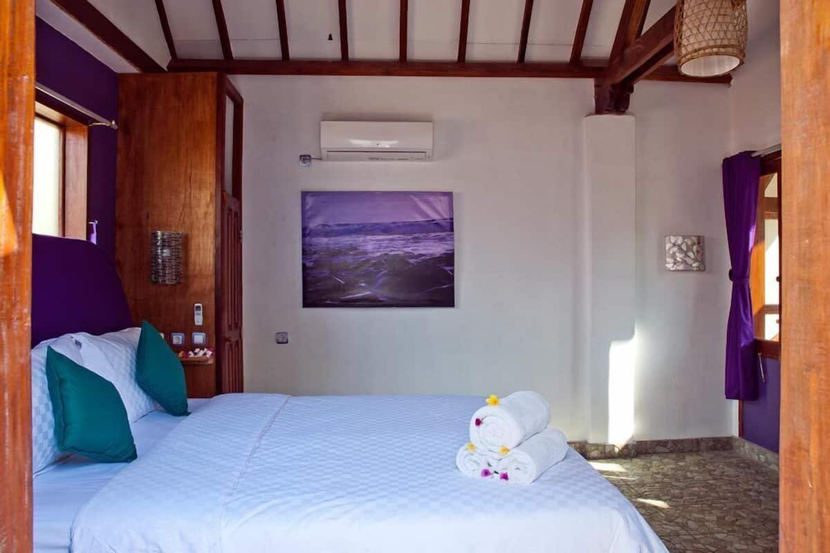 Hotelkamer met een bed, een schilderij, een wandairconditioner en een raam met gordijnen.